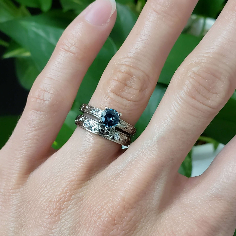 Engraved white gold Montana sapphire ring stacked with matching bands on hand