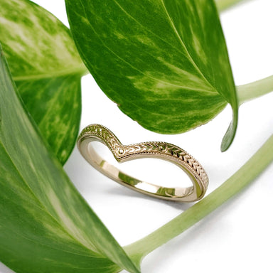 Engraved yellow gold chevron wedding ring nestled among green leaves