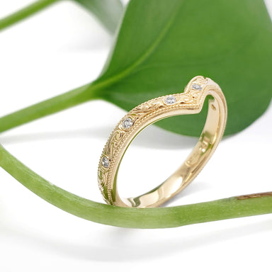 Engraved yellow gold chevron wedding ring with diamonds, styled on a green leaf