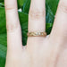 Engraved yellow gold diamond wedding ring worn on hand, green leaves background