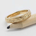 Engraved yellow gold wedding ring with millgrain, shown on a pencil