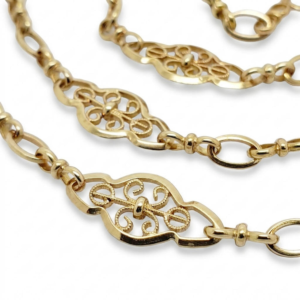 Gold chain necklace with ornate filigree center links and small oval beads, shown on a white background.