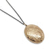 An oval gold locket pendant necklace with an engraved floral pattern, hanging from a thin black chain against a plain white background.