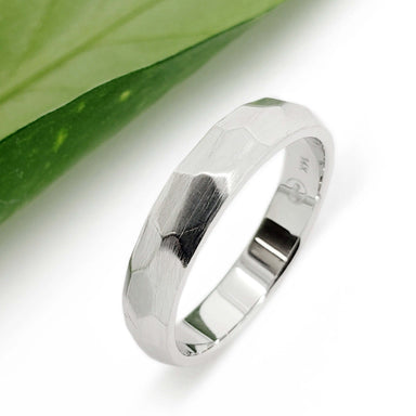 Faceted 14kt white gold wedding band with matte brushed finish beside a leaf