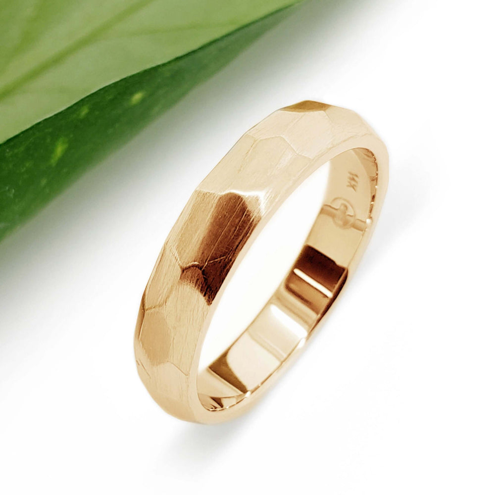 Faceted 14kt yellow gold wedding ring with matte brushed finish beside green leaf