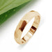 Faceted 14kt yellow gold wedding ring with matte brushed finish beside green leaf