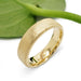 Flat 14kt yellow gold wedding ring with saw blade texture beside a green leaf