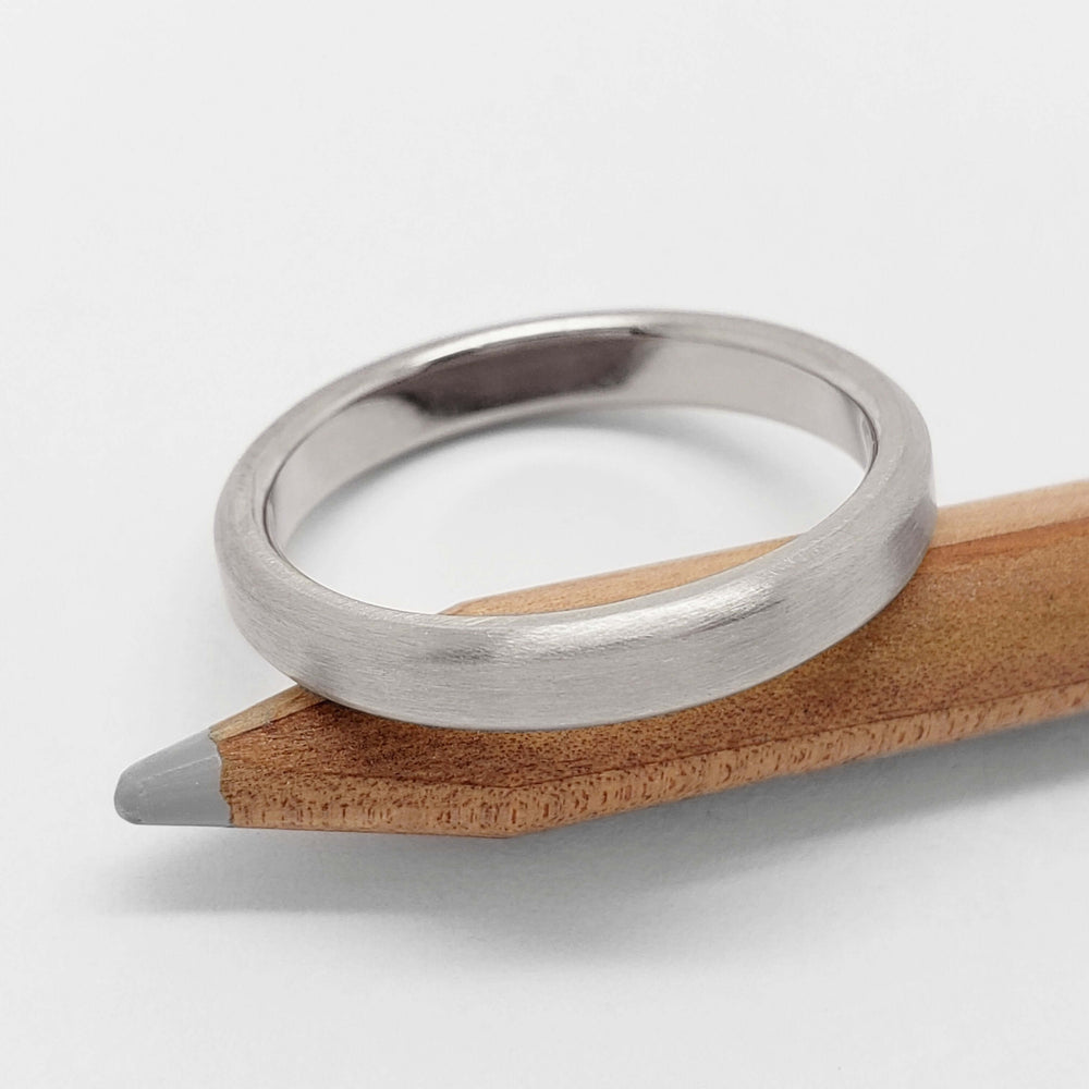 Flat brushed 14k white gold wedding ring resting on a wooden pencil