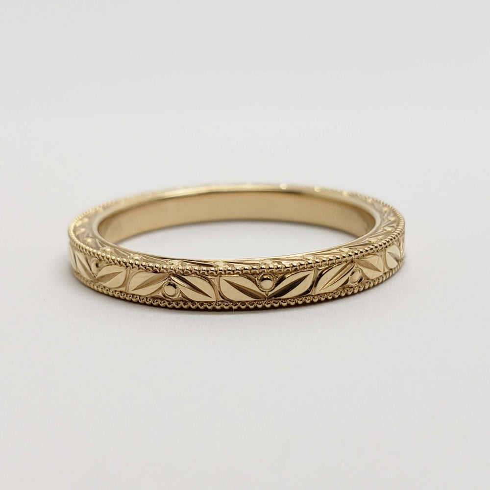 Flat lay of 14kt yellow gold wedding ring featuring engraved Salal leaf and berry motif and millgrain