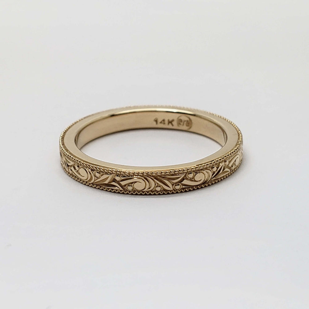 Flat lay of 14kt yellow gold wedding ring with detailed scroll engraving and millgrain