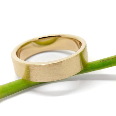 Flat profile 14kt yellow gold brushed wedding ring resting on a green stem