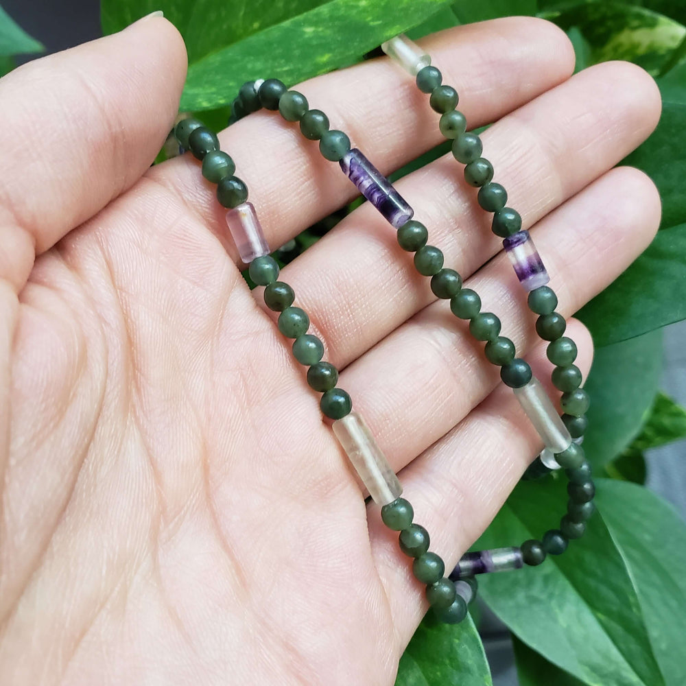 Hand holding a fluorite and serpentine bead necklace with green and purple tones