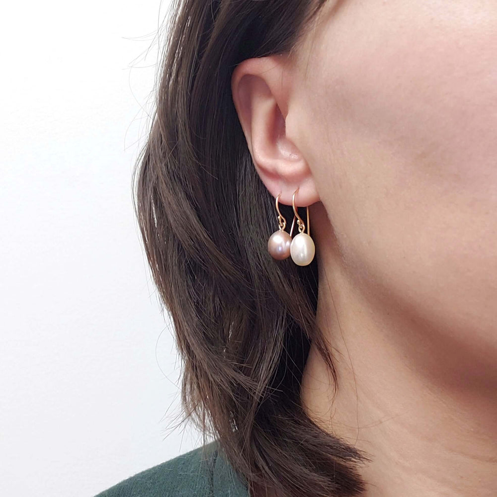 Model wearing mauve and white freshwater pearl dangle earrings with 14kt yellow gold hooks