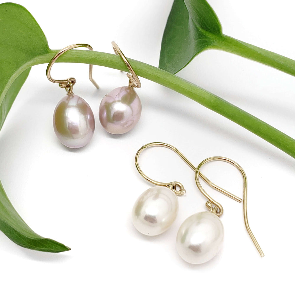 Freshwater pearl dangle earrings in mauve and white on 14kt yellow gold hooks, styled with green leaves