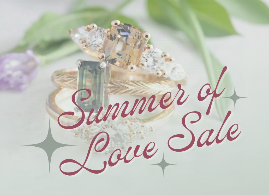 A promotional sale graphic featuring stacked rings with gemstones, overlaid with the text 'Summer of Love Sale' in cursive script with starburst accents on a soft light background.