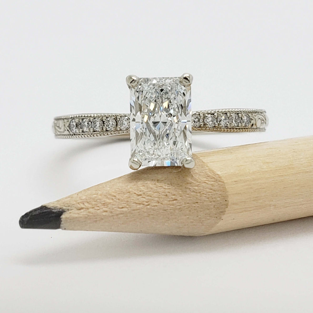 Front view of 14kt white gold engagement ring with radiant lab diamond and pave-set diamonds, next to pencil