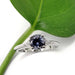 Front view of 14kt white gold ring with blue-grey spinel and triangle diamonds beside a green leaf
