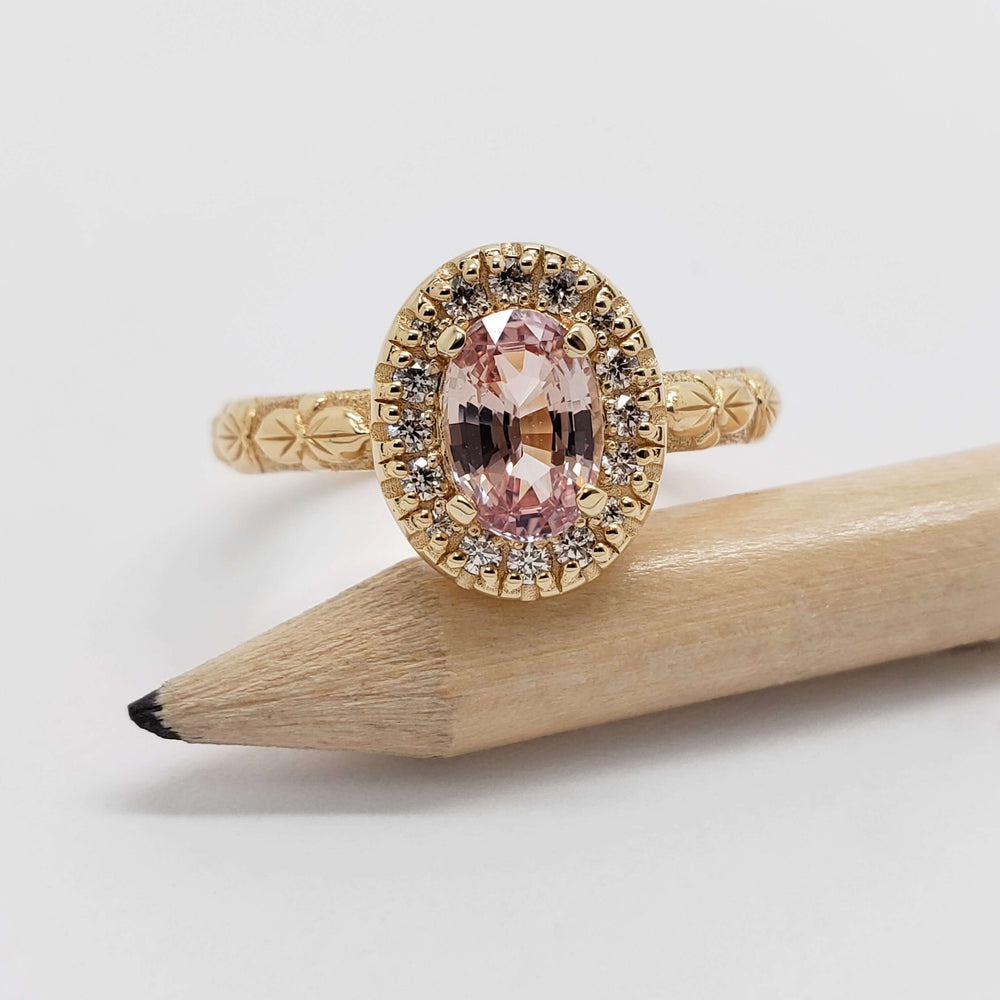 Front view of 14kt yellow gold ring with oval peach sapphire and diamond halo, engraved floral details