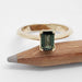 Front view of 14kt yellow gold ring with emerald cut green Tanzanian sapphire beside pencil