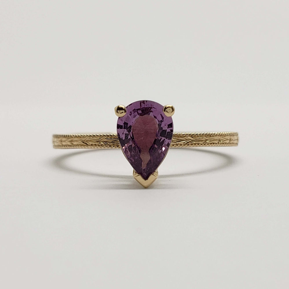 Front view of 14kt yellow gold ring with pear shaped pink sapphire and detailed engraving