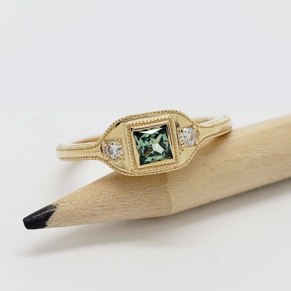 Front view of 14kt yellow gold ring with green lab sapphire and diamonds, resting on pencil