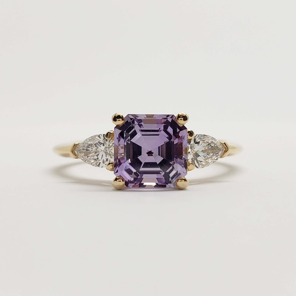 Front view of 14kt yellow gold ring with asscher cut lavender sapphire and pear lab diamonds