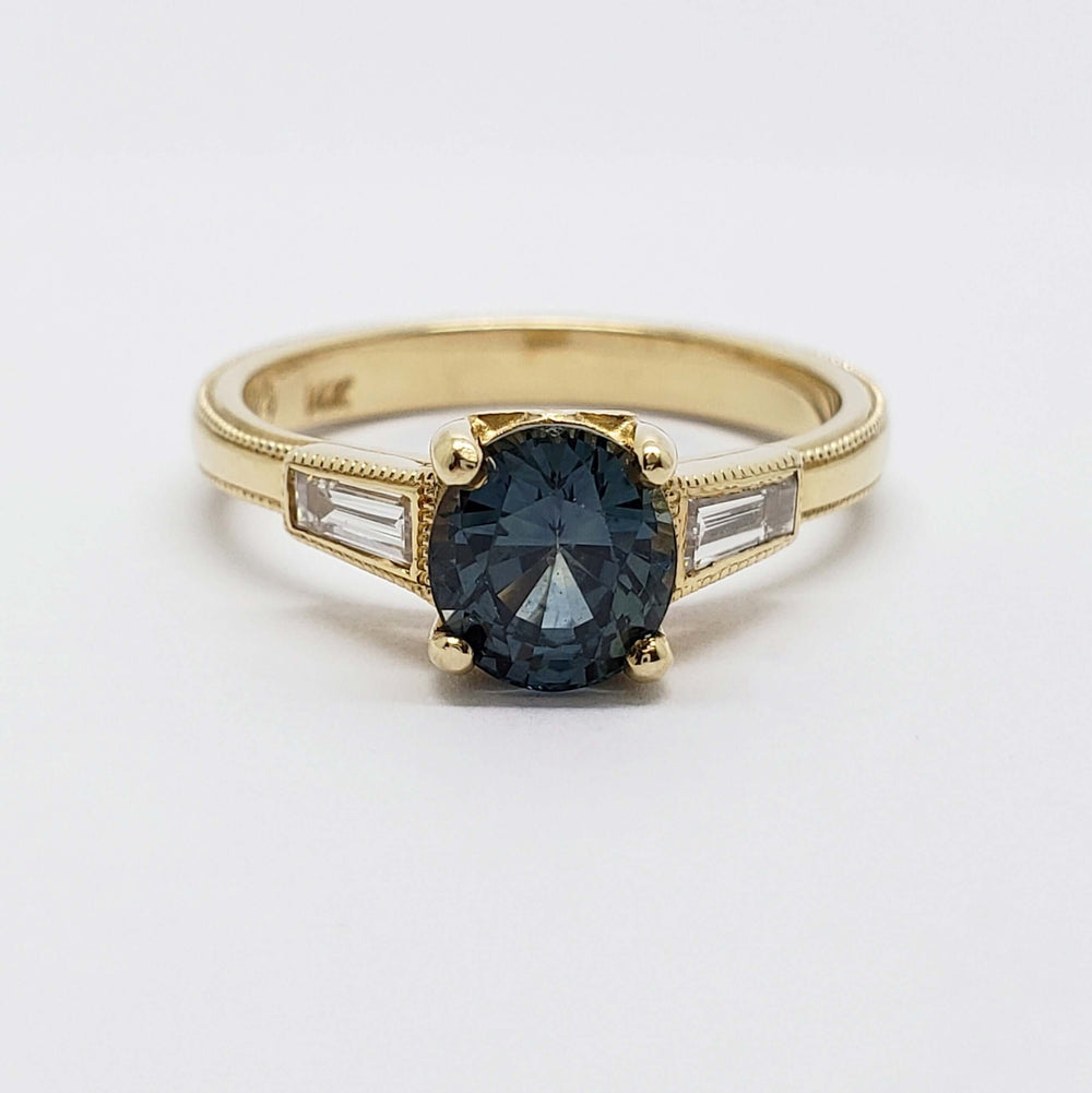 Front view of 14K yellow gold ring with teal Montana sapphire and baguette diamond accents