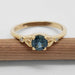 Front view of teal Montana sapphire and diamond yellow gold ring resting on a pencil