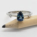 Front view of white gold ring with pear-shaped teal sapphire and two princess cut diamonds