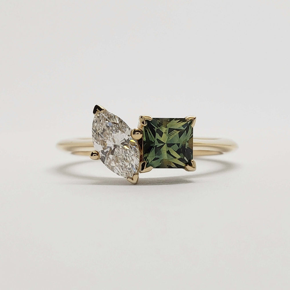 Front view of yellow gold ring with marquise diamond and princess cut teal sapphire