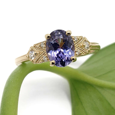 Front view of 14kt yellow gold ring with oval sapphire and diamond details on a leaf