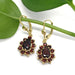 14kt yellow gold garnet dangle earrings with pear and round garnets, displayed on a green leaf