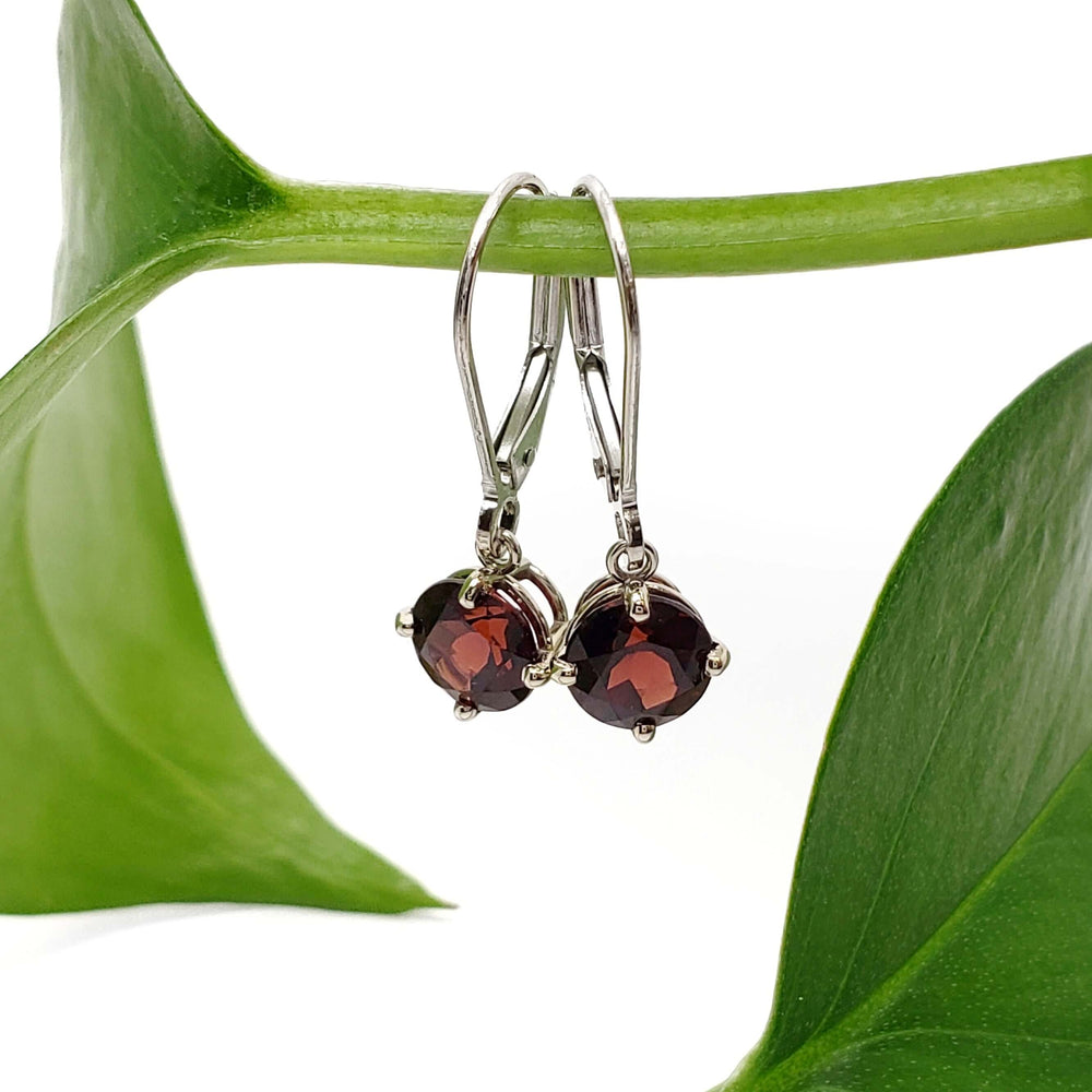 14kt white gold garnet drop earrings hanging from a green plant stem