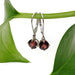 14kt white gold garnet drop earrings hanging from a green plant stem