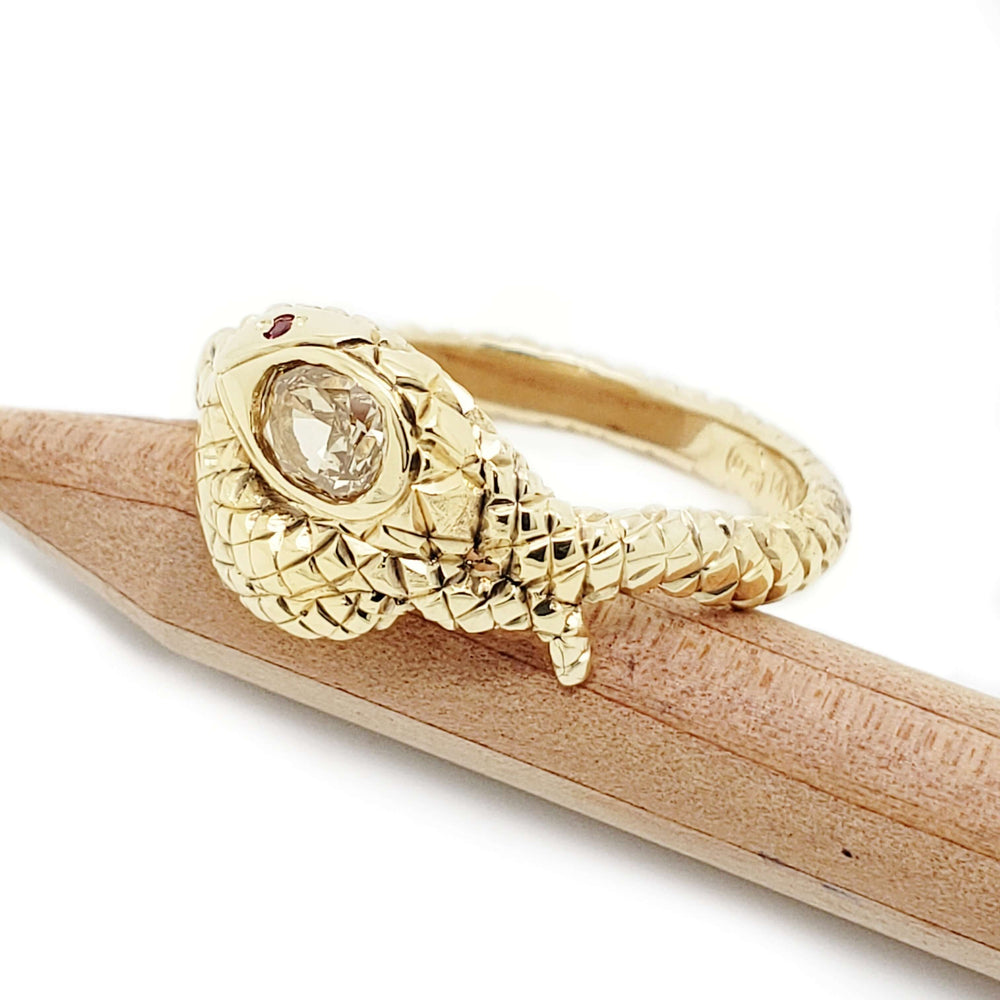 Side view of gold snake ring with champagne diamond and ruby eyes, on pencil