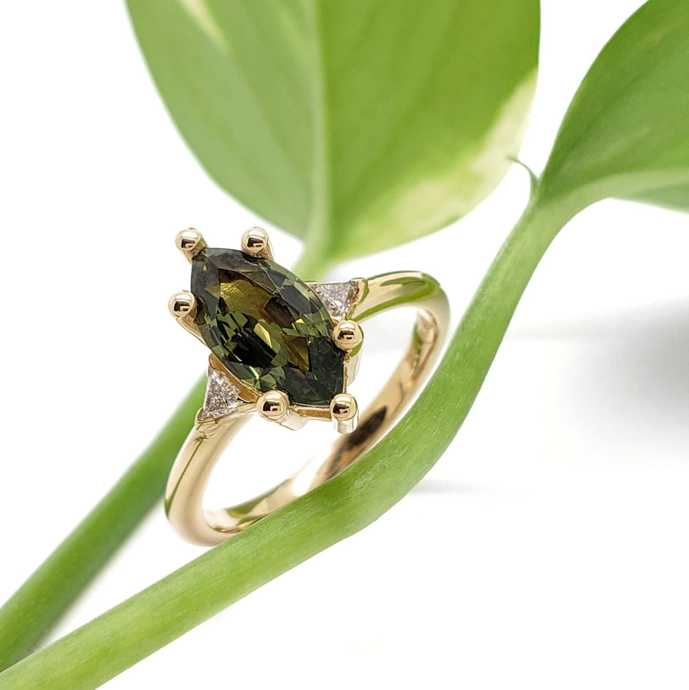 Green sapphire and lab diamond engagement ring in yellow gold, styled with plant