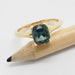 Green sapphire and yellow gold engagement ring displayed on a pencil