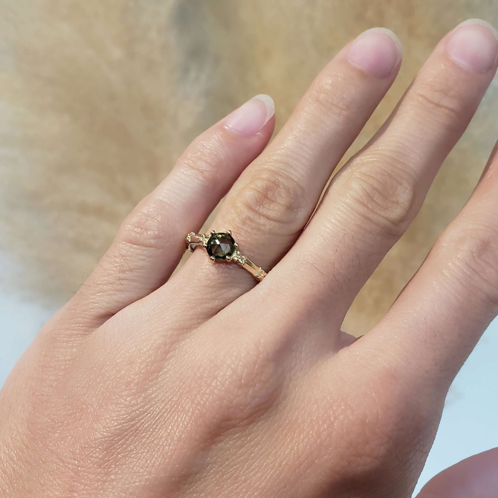 Green sapphire and yellow gold floral engagement ring shown on a hand