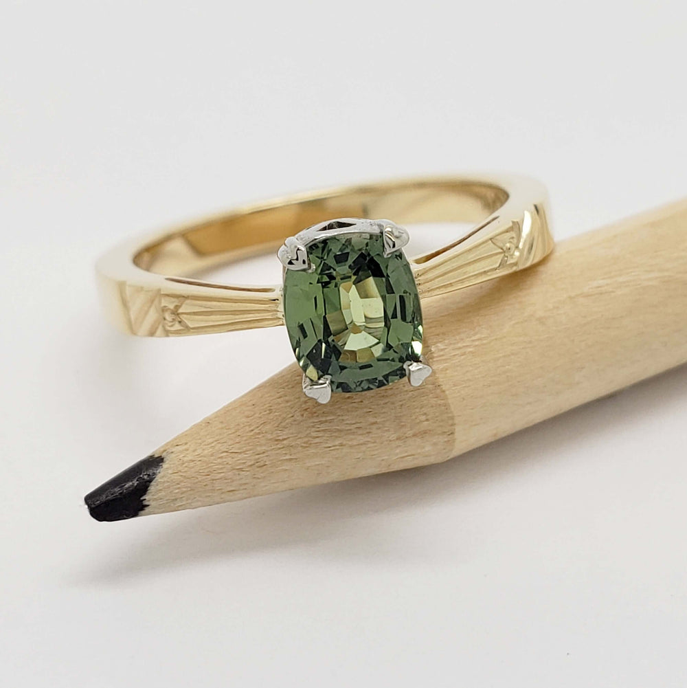 Green sapphire engagement ring in yellow and white gold, displayed on a pencil