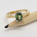Green sapphire engagement ring in yellow and white gold, displayed on a pencil