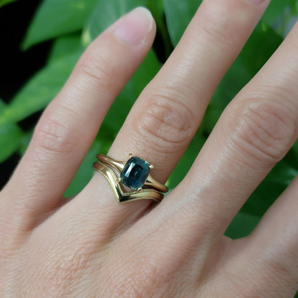 Green sapphire engagement ring in yellow gold stacked with chevron bands on hand