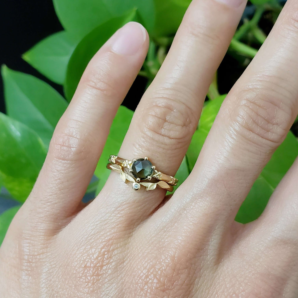 Green sapphire engagement ring stacked with a leaf motif band on a hand