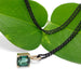 Barrel cut green tourmaline pendant in yellow gold with black chain, styled on green leaves