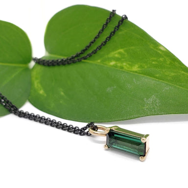 Green tourmaline baguette pendant in yellow gold on black chain with green leaf background