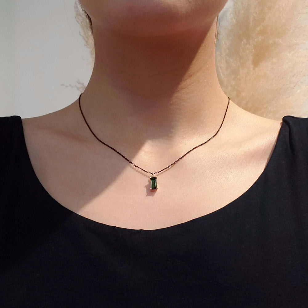 Baguette cut green tourmaline pendant in yellow gold worn on a black chain