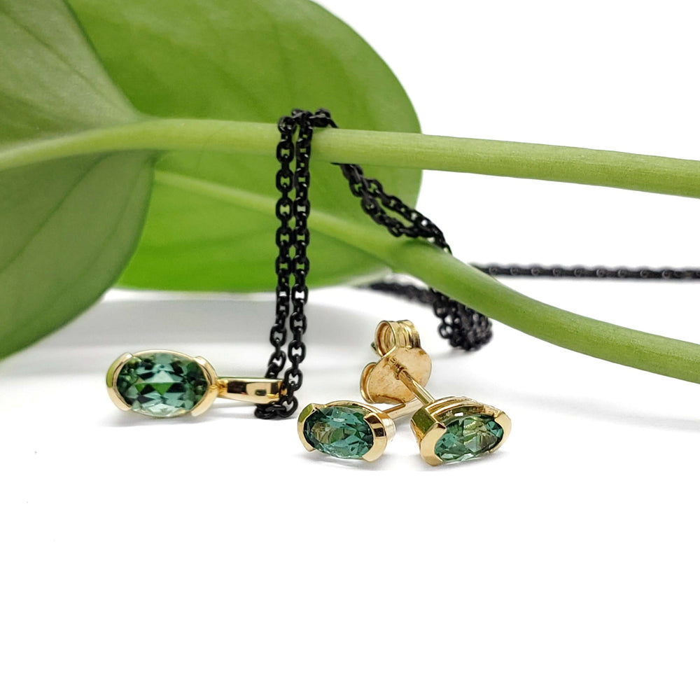 Green tourmaline oval pendant and earrings in 14kt yellow gold displayed with a leaf