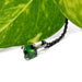 Green tsavorite garnet pendant in white gold with black chain, shown near leaf
