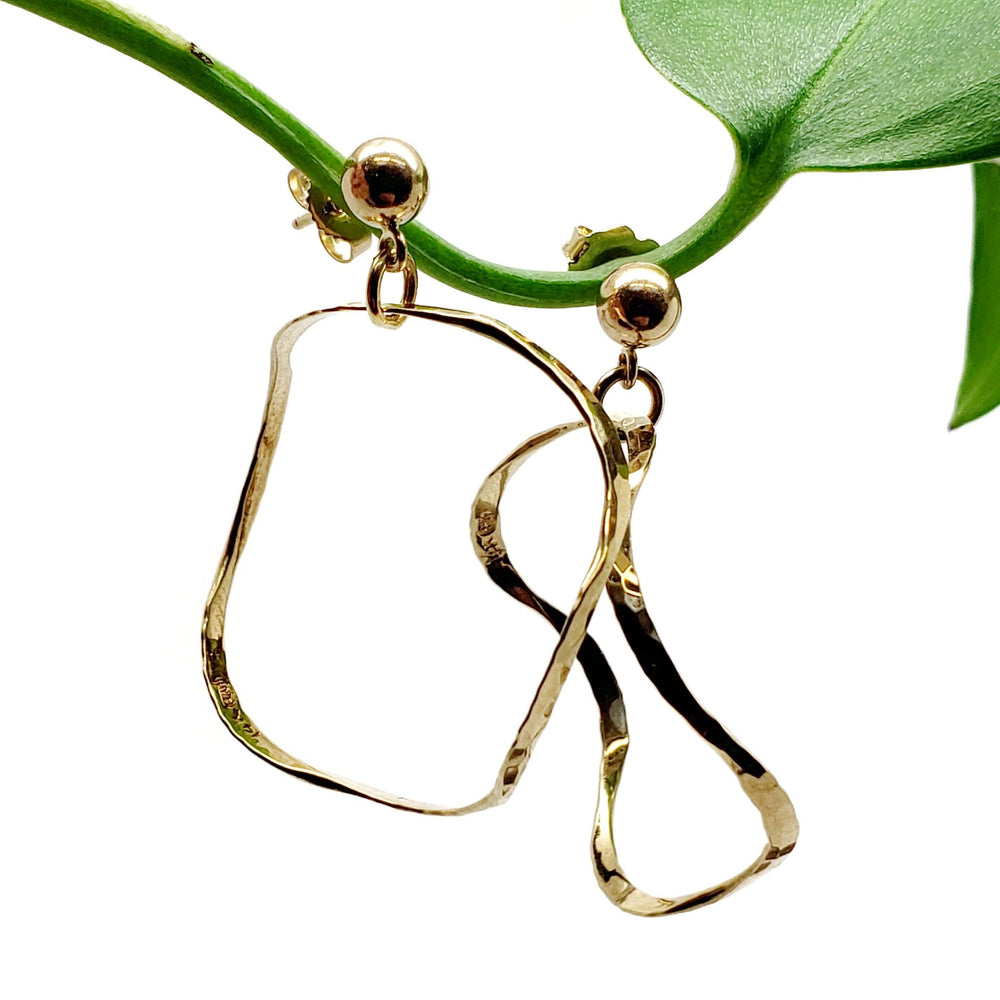 Vintage hammered 14kt yellow gold squiggle hoop earrings hanging from a green plant stem