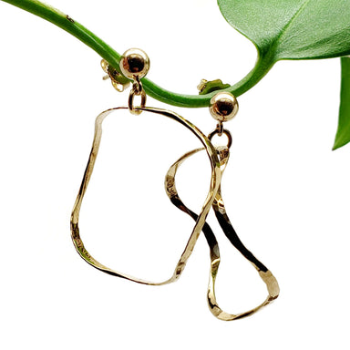 Vintage hammered 14kt yellow gold squiggle hoop earrings hanging from a green plant stem