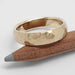 Hammered 14kt yellow gold wedding ring resting on a wooden pencil
